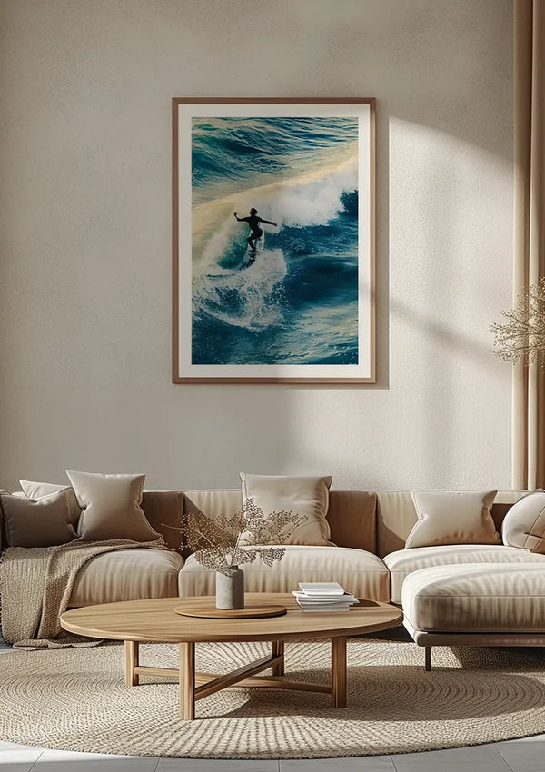 Een minimalistische woonkamer is voorzien van een beige sectionele bank met talloze kussens, een ronde houten salontafel en een groot ingelijst Surfer In Actie Schilderij van CollageDepot aan de muur. Bleke, neutrale tinten domineren het decor, aangevuld met zachte verlichting.,Lichtbruin