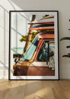 Een ingelijste foto van een vintage, roestkleurig busje met surfplanken op het dak, leunend tegen een lichtgekleurde muur. Dit charmante stukje wanddecoratie legt de voorruit en deur van het voertuig vast, met bomen en zonlicht op de achtergrond. Het Busje Met Surfborden Schilderij van CollageDepot rust elegant op een houten vloer.,Zwart