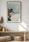Een ingelijste foto van een surfer die op een golf rijdt, wordt aan de muur boven een houten bank gehangen en dient als prachtige wanddecoratie. Het tafereel bevat decoratieve voorwerpen zoals gedroogd gras in een vaas, gestapelde mosterd- en beige kaarsen en ronde geweven kussens die onder de bank zijn geplaatst. Het "Surfer in Action Schilderij" van CollageDepot geeft een verkwikkende toets aan het decor.,Lichtbruin