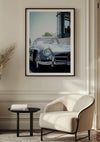 Een ingelijst CollageDepot Mercedes 300SL Schilderij hangt aan een muur boven een witte, moderne fauteuil en een klein zwart bijzettafeltje in een minimalistische woonkamer. Natuurlijk licht stroomt van rechts naar binnen en creëert zachte schaduwen op de lichtgekleurde muur en vloer, wat deze elegante wanddecoratie perfect aanvult.,Zwart