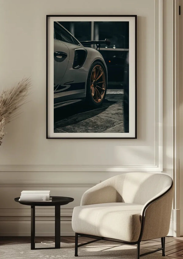 Een opvallend Porsche GT3 RS Schilderij van CollageDepot hangt als stijlvolle wanddecoratie aan de muur. Aan de voorkant staat een beige moderne fauteuil naast een ronde bijzettafel met een klein decoratief item, allemaal prachtig gerangschikt in een kamer met houten vloer.,Zwart