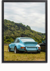 Een ingelijste foto toont een Babyblauw Porsche 911 Schilderij geparkeerd op gras, met een beboste heuvel op de achtergrond. De auto heeft een grote achterspoiler en brede banden, terwijl een ander voertuig gedeeltelijk zichtbaar is. Deze wanddecoratie van CollageDepot wordt geleverd met een magnetisch ophangsysteem voor eenvoudige weergave.,Zwart-Zonder,Lichtbruin-Zonder,showOne,Zonder