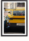 Een ingelijste foto van het achteraanzicht van een geel Porsche 911 GT3 RS schilderij. De auto heeft een grote achtervleugel en zichtbare motoropeningen, geparkeerd in een straat met gebouwen op de achtergrond. Op het kenteken staat 'Porsche'. Perfect als wanddecoratie, het Gele Porsche GT3 RS Schilderij van CollageDepot bevat een magnetisch ophangsysteem voor eenvoudige montage.,Zwart-Met,Lichtbruin-Met,showOne,Met