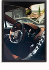 Een ingelijst CollageDepot Bugatti Chiron Interior Schilderij legt het interieur van een luxe auto vast. Het dashboard is voorzien van een stuur met het embleem van het merk, bruinleren bekleding en een rij bedieningsknoppen. De achtergrond bevat een wazig zicht op het buitenlandschap, waardoor het een perfecte luxe wanddecoratie is voor thuis of op kantoor.