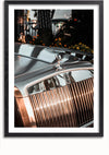 Een ingelijste foto van een Rolls Royce Grille En Embleem Schilderij toont de voorkant van een vintage auto, met een close-up van de grille en het motorkapornament. De metalen grille heeft verticale lamellen en het motorkapornament steekt opvallend af tegen het gepolijste oppervlak van de auto. Ideale wanddecoratie met magnetisch ophangsysteem voor eenvoudige plaatsing vanuit CollageDepot.,Zwart-Met,Lichtbruin-Met,showOne,Met