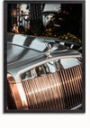 Close-up van de voorkant van een zilveren luxeauto, waarbij de iconische grille en het motorkapornament prominent zichtbaar zijn. De achtergrond bestaat uit wazig gebladerte en wat licht, waardoor een contrasterende omgeving ontstaat. De foto is ingelijst in een zwarte rand, waardoor hij perfect geschikt is als Rolls Royce Grille En Embleem Schilderij van CollageDepot met een magnetisch ophangsysteem.,Zwart-Zonder,Lichtbruin-Zonder,showOne,Zonder