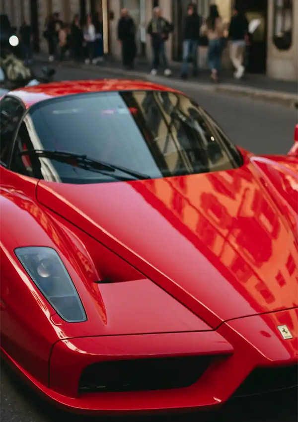 Een rode CollageDepot aaa 043 - auto geparkeerd op straat, met zijn opvallende strakke lijnen en Ferrari-logo zichtbaar. De achtergrond toont een drukke stadsomgeving met voetgangers.-