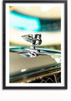 Close-up van een Bentley-embleem in de vorm van een gevleugelde "B". Het glanzende metalen embleem reflecteert het licht en benadrukt het gedetailleerde ontwerp. De onscherpe achtergrond vertoont onduidelijke vormen en kleuren. De afbeelding is ingelijst in een eenvoudige zwarte lijst met een magnetisch ophangsysteem voor eenvoudige weergave. Dit is het Prachtig Bentley Embleem Schilderij van CollageDepot.,Zwart-Met,Lichtbruin-Met,showOne,Met