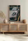 Een Nardo Grey Porsche 718 Schilderij van CollageDepot is gemonteerd boven een lichtgekleurd houten dressoir met rotan kastdeuren. Op het dressoir staat een beige keramische vaas met gedroogd pampasgras, een lichtbruine bolvormige vaas en een kleine stapel boeken, waardoor de perfecte wanddecoratie ontstaat.,Lichtbruin