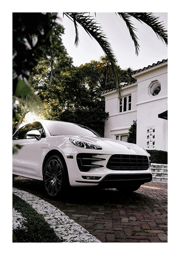 Een witte luxe SUV van CollageDepot geparkeerd op een geplaveide oprit voor een luxe wit huis, omlijst door palmbladeren op de voorgrond.-