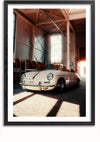 Een ingelijste foto van een witte vintage cabriolet die binnen geparkeerd staat en het licht door een groot raam naar binnen stroomt. Aan de linkerkant van de ruimte staan wijnvaten opgesteld, waardoor een ideale wanddecoratie ontstaat. De scène heeft een warme en nostalgische sfeer, die doet denken aan een Witte Porsche 356 Cabriolet Schilderij van CollageDepot.,Zwart-Met,Lichtbruin-Met,showOne,Met