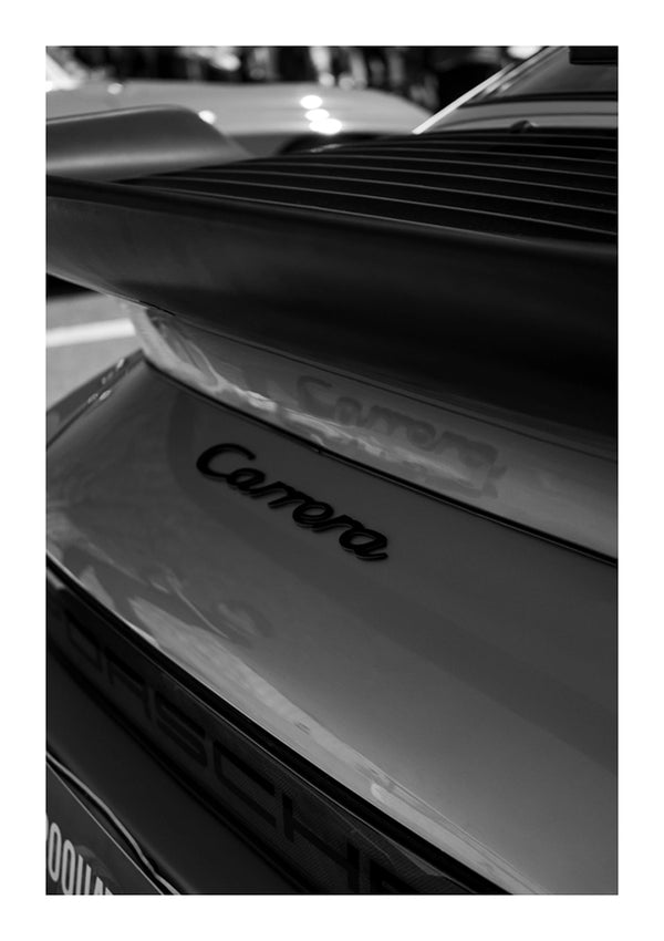 Close-up zwart-witfoto van de achterkant van een CollageDepot Porsche Carrera 074, met de nadruk op het "Carrera" embleem. De afbeelding benadrukt de strakke lijnen en contouren van het ontwerp van de auto.-