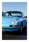 Een vintage blauwe CollageDepot aaa 086 - auto geparkeerd in fel zonlicht, met zijn gepolijste carrosserie en ronde koplampen, met een onscherpe achtergrond die de auto benadrukt.-
