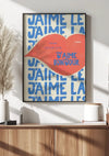 Aan de muur hangt een ingelijste poster met de woorden "J'aime le J'aime Bonjour" in blauwe tekst, met een grote rode tekstballon over een deel van de tekst heen. Het CollageDepot J'aime Le Bonjour Schilderij rust op een houten console met decoratieve items, waaronder een gedroogde plant en vaas, met behulp van een magnetisch ophangsysteem voor gemakkelijke weergave.,Zwart