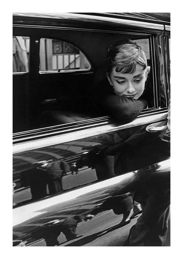 Een zwart-wit portret van een vrouw die haar kin op haar hand laat rusten en uit het raam van een klassieke auto leunt, wat een weemoedige blik geeft, met stadsreflecties zichtbaar op het glanzende oppervlak van de auto. Deze afbeelding is gemaakt met CollageDepot's ab 015 - zwart-wit.-