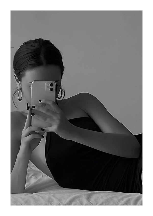ab 027 - zwart-wit foto door CollageDepot van een vrouw die op bed ligt, wegkijkend van de camera en een selfie maakt met haar smartphone. Ze draagt een donker mouwloos topje en heeft haar haar in een interieursetting naar achteren gebonden.-