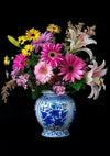 Een decoratieve blauw-witte keramische vaas bevat een kleurrijk bloemenarrangement met roze gerberamadeliefjes, gele margrietachtige bloemen en witte lelies, afgezet tegen een zwarte achtergrond zoals het CollageDepot Delfts Blauw Bloemen In Vaas Schilderij.