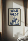 Een ingelijst "Wild West Schilderij" met een cowboy op een paard hangt als boeiende wanddecoratie aan de muur. De kamer wordt zacht verlicht en het zonlicht valt door de gordijnen naar binnen, wat de schoonheid van de tentoongestelde kunstwerken benadrukt. Op de voorgrond is een deel van een bed met wit beddengoed zichtbaar. Dit prachtige stuk is van CollageDepot.,Zwart
