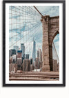 Foto van de Brooklyn Bridge met zijn ophangkabels die een zicht geven op verschillende gebouwen in de skyline van New York City, waaronder het One World Trade Center, onder een gedeeltelijk bewolkte hemel. De afbeelding is ingesloten in een zwarte fotolijst en is voorzien van een magnetisch ophangsysteem voor eenvoudige weergave. Dit is het schilderij Uitzicht Skyline New York van CollageDepot.,Zwart-Met,Lichtbruin-Met,showOne,Met