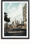 Foto van een stadsgezicht met een prominente wolkenkrabber in het midden, omlijst door palmbomen en moderne gebouwen aan beide zijden. De weg op de voorgrond leidt naar de wolkenkrabber. De afbeelding, perfect voor wanddecoratie, is gevat in een zwarte lijst. Introductie van het Skyline Dubai schilderij van CollageDepot.