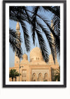 Een foto van een moskee met drie minaretten en een prominente koepel, omlijst door palmbladeren op de voorgrond. De lucht is helder en blauw en vormt een contrast met de beige architectuur. De foto, die doet denken aan een ingewikkeld schilderij, is gevat in een zwarte lijst. Dit prachtige stuk getiteld "Moskee Met Sierlijke Structuur Schilderij" van CollageDepot voegt een elegante toets toe aan elke ruimte.,Zwart-Met,Lichtbruin-Met,showOne,Met