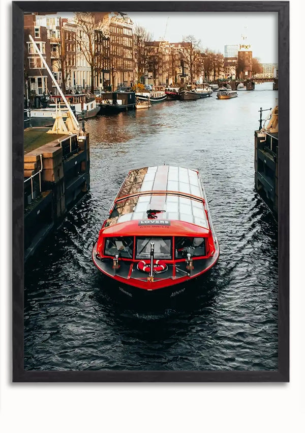 Een rode Rondvaartboot In Amsterdam Schilderij van CollageDepot met een transparant dak vaart door een gracht omgeven door gebouwen aan weerszijden. Passagiers zijn zichtbaar binnen en genieten van het stedelijke landschap. Het kanaal, omzoomd met bomen en afgemeerde boten, vormt een schilderachtig decor voor deze charmante waterwegtocht.,Lichtbruin