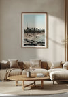 Een minimalistische woonkamer is voorzien van een beige bank met bijpassende kussens, een ronde houten salontafel en een groot ingelijst Skyline Dubai Schilderij van CollageDepot. Zonlicht stroomt door een onzichtbare bron naar binnen en werpt schaduwen op de muur.,Lichtbruin