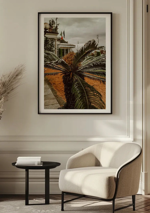Aan een crèmekleurige muur boven een witte fauteuil hangt een ingelijste foto van een palmplant. Naast de stoel staat een zwarte ronde bijzettafel met een stapel boeken. Links is een pampasgras-arrangement zichtbaar. De ruimte is gevuld met natuurlijk licht, aangevuld met bbb 021 - natuur van CollageDepot.,Zwart