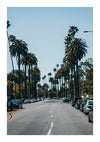 Er wordt een brede straat getoond met aan weerszijden hoge palmbomen, perfect voor een CollageDepot Stadstraat Met Hoge Palmbomen Schilderij als wanddecoratie. Geparkeerde auto's bezetten beide zijden van de weg en in de verte zijn enkele voertuigen te zien rijden. De lucht is helder en blauw, ideaal voor weergave met een magnetisch ophangsysteem.-
