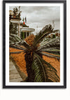 Een ingelijste foto toont een close-up van een palmachtige plant met gevederde bladeren. Op de achtergrond is er een gebouw versierd met vlaggen, bomen en een bewolkte lucht. De setting lijkt een buitenruimte te zijn met een oranje getint pad of terrein. De foto heet bbb 021 - natuur en is afkomstig van CollageDepot.,Zwart-Met,Lichtbruin-Met,showOne,Met