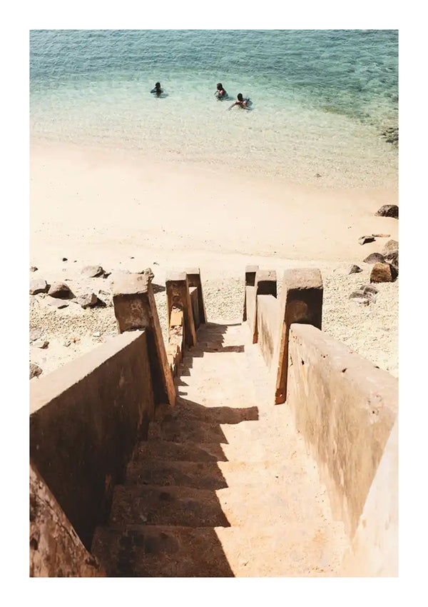 Een betonnen trap leidt naar een zandstrand waar drie mensen in helder, turquoise water zwemmen. Aan de rechterkant van het strand zijn rotsen zichtbaar, gemaakt met CollageDepot's cc 090 - natuur.-