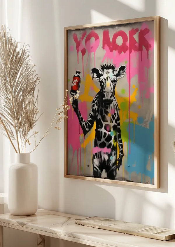 Aan de muur hangt een ingelijst schilderij Giraffe Met Spuitbus van CollageDepot. De giraffe heeft een mensachtige houding tegen een kleurrijke, graffiti-achtige achtergrond met de woorden "YO LOVE" bovenaan gespoten. Op een plank eronder staat een vaas met gedroogde planten, vastgezet door een magnetisch ophangsysteem.,Lichtbruin