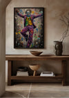 Een ingelijst, kleurrijk Kleurrijk Joker-schilderij van CollageDepot van een dansende figuur verkleed als clown hangt aan een beige muur boven een houten consoletafel. Op de tafel staan decoratieve kommen, gestapelde boeken en een keramische vaas met kale takken. De vloer is voorzien van een licht marmerpatroon.,Zwart