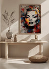 Een minimalistisch interieur met een kleurrijk Marilyn Monroe-schilderij van CollageDepot boven een houten consoletafel. Op de tafel staan twee vazen, een schaaltje, gestapelde boeken en een decoratieve tak. Naast de tafel ligt een rond kussen op de grond.
