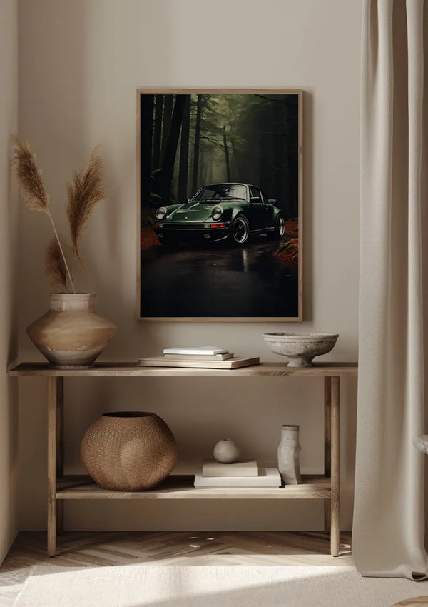 Aan een beige muur wordt een CollageDepot wanddecoratie met The Green Mile Schilderij van een groene klassieke 911 in een bosrijke omgeving gehangen. Daaronder staat op een houten plank een grote vaas met gedroogde planten, een rieten mand, een glazen container, twee kommen en een klein wit ornament.,Lichtbruin