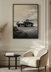 De afbeelding toont een ingelijste zwart-witfoto van een Zwart-wit 911 Schilderij van CollageDepot aan een muur. Onder de wanddecoratie staat een moderne witte stoel en een kleine ronde zwarte tafel in een minimalistische kamer met lichtgekleurde muren en een smaakvolle inrichting.,Zwart
