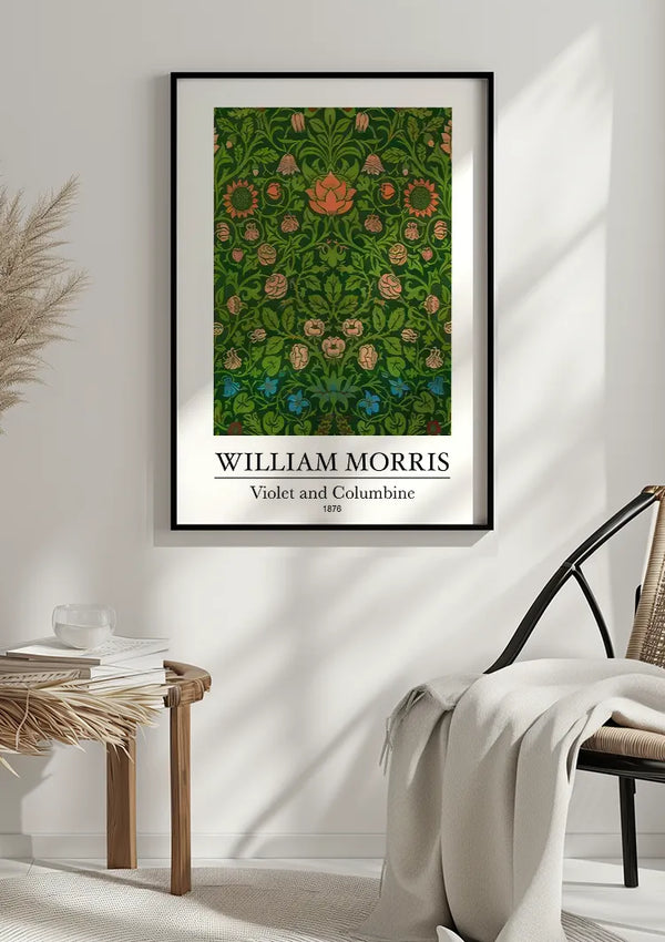 Een ingelijst CollageDepot W. Morris Violet And Columbine Schilderij getiteld "William Morris: Violet and Columbine, 1876" hangt aan een witte muur als elegante wanddecoratie. Het ontwerp bevat ingewikkelde bloempatronen in groen, met accenten in rood, blauw en roze. Onder het frame staat een tafel met boeken en een plant, en een stoel met een deken ernaast.,Zwart