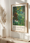 Een ingelijste reproductie van Gustav Klimt's "Boerderij met Zonnebloemen" uit 1907, het Gustav Klimt Boerderijtuin met Zonnebloemen Schilderij van CollageDepot, hangt als een prachtige wanddecoratie aan een witte muur. Het kunstwerk toont een weelderige tuin met levendige zonnebloemen en andere kleurrijke bloemen. Links staat elegant een witte vaas met gedroogd pampagras.,Lichtbruin