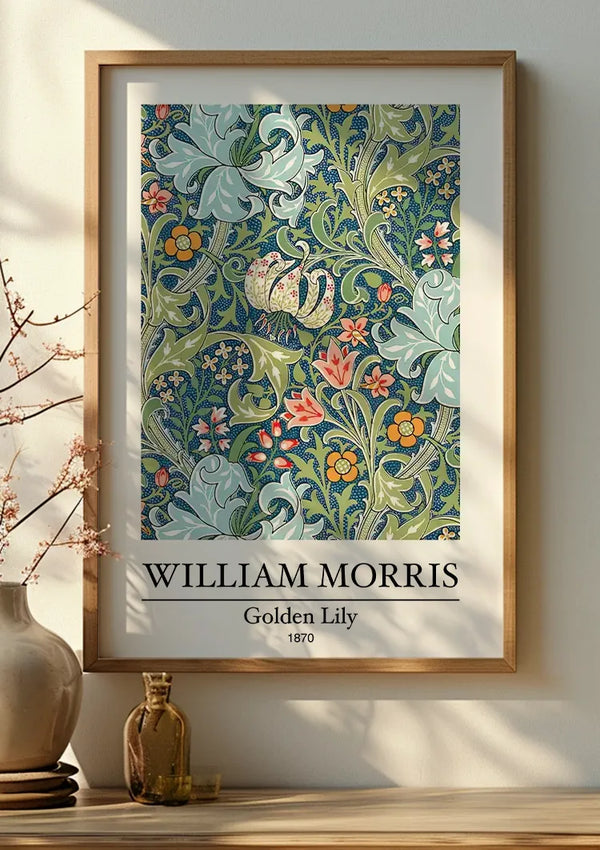 Een ingelijst W. Morris Golden Lily Schilderij van CollageDepot toont een ingewikkeld bloemmotief met de titel "Golden Lily" van William Morris uit 1870. Met groene wijnstokken, bladeren en verschillende bloemen in de kleuren blauw, roze en geel zit dit stuk wanddecoratie op een houten oppervlak bij een vaas met takken. Het schilderij wordt vastgehouden met een magnetisch ophangsysteem voor eenvoudige montage.,Lichtbruin