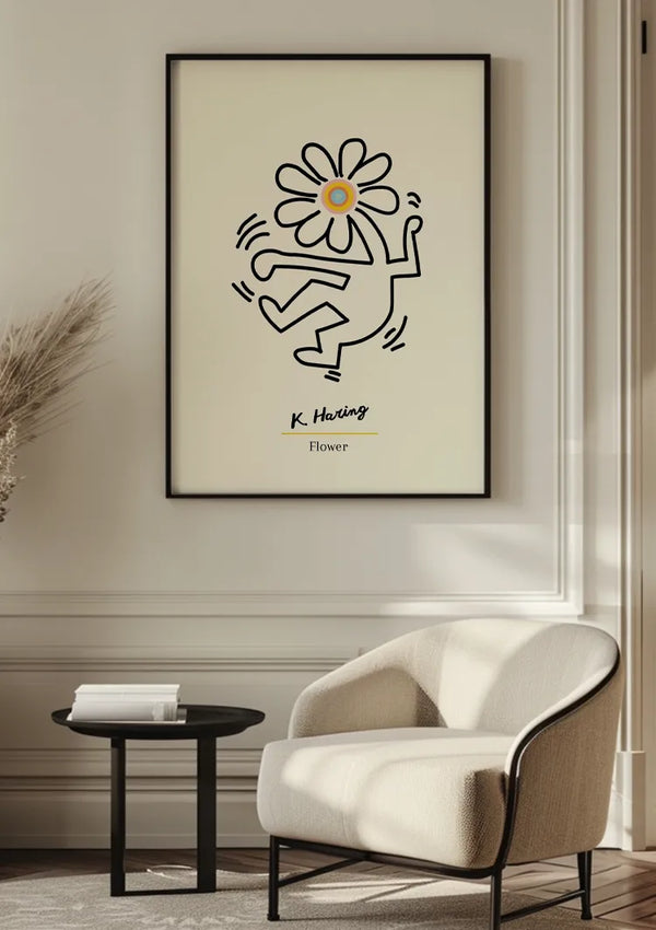 Een ingelijste **K. Haring - Bloem Illustratie Schilderij** van **CollageDepot** met een simplistische, cartoonachtige figuur met een bloem als hoofd, wordt aan de muur gehangen met behulp van een magnetisch ophangsysteem. Onder de figuur staat de tekst "K. Haring" en "Bloem." Vooraan staat een crèmekleurige moderne fauteuil en een klein zwart bijzettafeltje.,Zwart