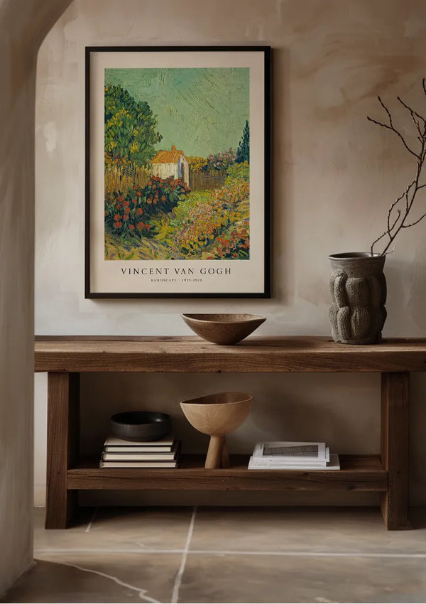 Een ingelijste CollageDepot V. Van Gogh Weelderige Tuin Schilderij hangt aan een beige muur boven een houten consoletafel. Op de tafel staan een kom, een vaas en een paar boeken. Het decor straalt een rustieke en minimalistische esthetiek uit. Een gebogen ingang omlijst gedeeltelijk de linkerkant, wat de algehele charme van deze wanddecoratie versterkt.,Zwart