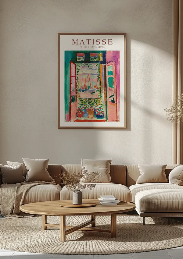 Een woonkamer met een groot ingelijst Matisse-kunstwerk met de titel "The Cut-Outs" aan de muur. De kamer is voorzien van een beige bank met witte kussens, een ronde houten salontafel en een lichtbruin vloerkleed. Op de tafel staat een gedroogd bloemstuk en het schilderij maakt gebruik van een CollageDepot magnetisch ophangsysteem voor eenvoudige wanddecoratie van hun Matisse - The Cut Outs Open Window Schilderij.,Lichtbruin
