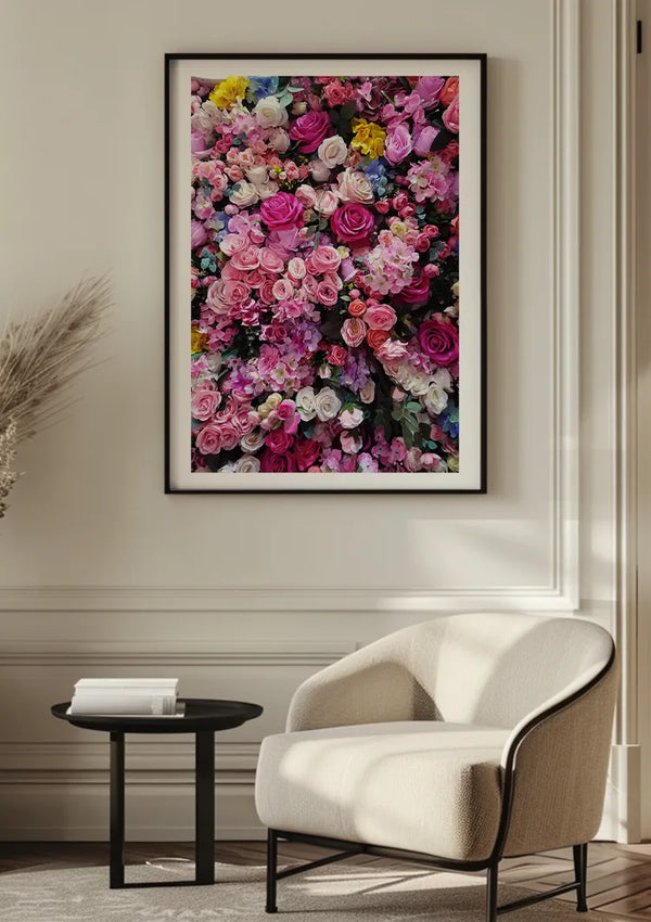 Een moderne, minimalistische kamer met een witte fauteuil, een klein zwart rond bijzettafeltje en het Roze Bloemen Schilderij van CollageDepot met een groot ingelijst bloemkunstwerk aan de muur. De wanddecoratie toont levendige roze, witte en geelroze lelies. In de hoek is een gevederde plant zichtbaar.,Zwart