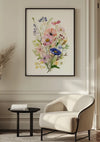 Een ingelijste botanische print, een prachtig voorbeeld van Bloemen Met Aquarel Schilderij van CollageDepot met kleurrijke bloemen, waaronder roze, paarse en blauwe bloemen, hangt aan een lichtgekleurde muur. Daaronder maken een crèmekleurige gestoffeerde stoel en een klein rond zwart bijzettafeltje de moderne, minimalistische wanddecoratie compleet.,Zwart