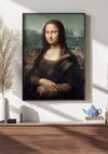 Een ingelijst portret van de Mona Lisa hangt aan een witte muur boven een houten oppervlak. Op het oppervlak staan een witte vaas met gedroogd gras, een stapel boeken, een blauw-witte theepot en een bijpassend theekopje. Het zonlicht stroomt naar binnen en werpt schaduwen. Het Leonardo Da Vinci Mona Lisa Schilderij van CollageDepot is voorzien van een magnetisch ophangsysteem voor eenvoudige weergave.