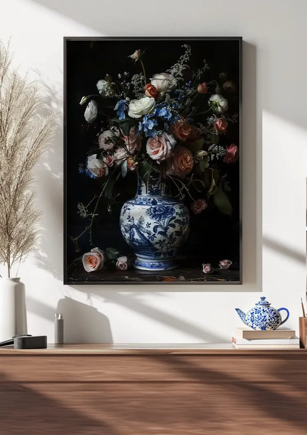 Aan een witte muur hangt een groot CollageDepot Delfts Blauw Rozen en Vaas Schilderij van een bloemstuk, inclusief een prachtig boeket rozen in een blauw-witte vaas. De wanddecoratie is voorzien van diverse bloemen en takken. Onder het schilderij bevindt zich een houten plank met decorartikelen, waaronder een theeketel en kopjesset, en een groot boeket van gedroogd gras.,Zwart