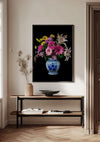 Een Delfts Blauw Bloemen In Vaas Schilderij van CollageDepot hangt aan een muur boven een houten consoletafel. Op de tafel staat een keramische vaas met gedroogde takken, een ondiepe schaal en een open boek. De kamer heeft een minimalistische inrichting met lichtgekleurde muren en houten vloeren, voorzien van een elegant bloemenarrangement.,Zwart