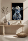 Een minimalistische kamer met een groot ingelijst kunstwerk van een koe bedekt met een blauw bloemmotief, hangend boven een houten consoletafel. Op de console staat een vaas met gedroogde takken en een kleinere vaas Aab 330 Delfts blauw van CollageDepot. Ervoor wordt een rond kussen geplaatst.,Lichtbruin
