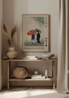 Een ingelijste Japanse print met de titel "O. Koson Rain in Japan Schilderij" van CollageDepot wordt op een muur boven een houten consoletafel getoond en dient als de perfecte wanddecoratie. De tafel is voorzien van decoratieve items, waaronder een vaas met pampasgras, een mand en een keramische kom. De setting is minimalistisch met neutrale tinten.,Lichtbruin