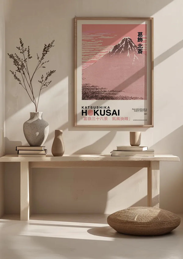 Het minimalistische interieur bestaat uit een houten bank met twee vazen en een boek. Boven de bank hangt een ingelijst K. Hokusai Fuji Bergen Bij Helder Weer Schilderij van CollageDepot, in een roze en rood kleurenschema. Schaduwen werpen op de lichtbeige muur achter de bank en versterken de elegante wanddecoratie met zijn rustgevende aanwezigheid.,Lichtbruin